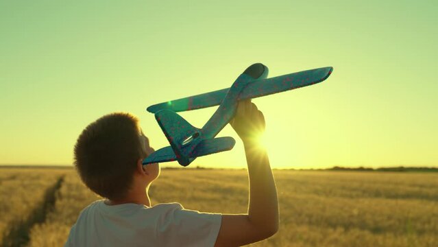 Child boy dreams of flying becoming pilot. Kid aviator. Happy child throws toy plane with his hand on field, sunset. Boy child wants to become pilot, astronaut. Slow motion. Children play toy airplane