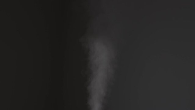 White rapid steam, smoke or fog rises straight up on dark background. Vapour stream generator. Evaporation from humidifier, air purifier, diffuser or teapot. Gas spraying, smog fumes