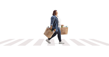 Corpulent woman with grocery bags crossing a street and walking at a pedestrian crosswalk