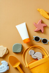 Tube of sunscreen cream with baby sunglasses and sand toys on color background.