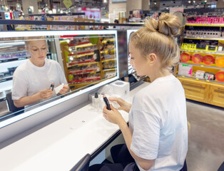 Woman buying make up at cosmetics section in store. choosing cosmetics, perfumes, creams and shampoos, Using tester.