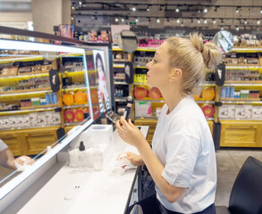 Woman buying make up at cosmetics section in store. choosing cosmetics, perfumes, creams and shampoos, Using tester.