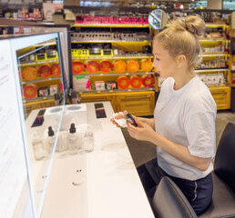 Woman buying make up at cosmetics section in store. choosing cosmetics, perfumes, creams and shampoos, Using tester.