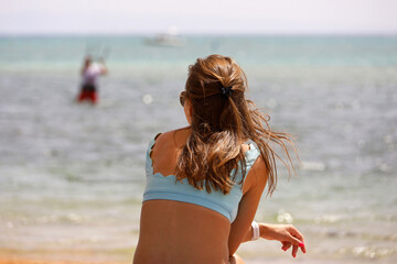 Naklejka premium Girl in swimsuit sitting on sea beach and looking at a man engaged in parasailing. Relaxation on summer resort