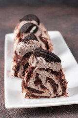 Sliced chocolate meringue roll with cookies on white plate on brown background