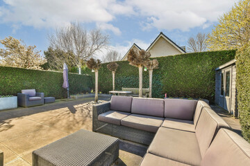 an outdoor living area with couches, tables and umbrellas on the patio in front of a green hedge...