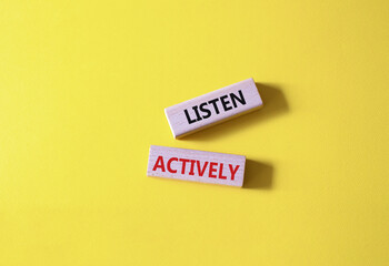 Listen actively symbol. Wooden blocks with words Listen actively. Beautiful yellow background. Business and Active listening concept. Copy space.