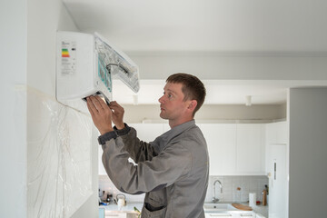 Man professional technician worker electrician in uniform installing air conditioner in modern apartment on wall on kitchen. Maintenance and repair service concept. Climate control, split system.