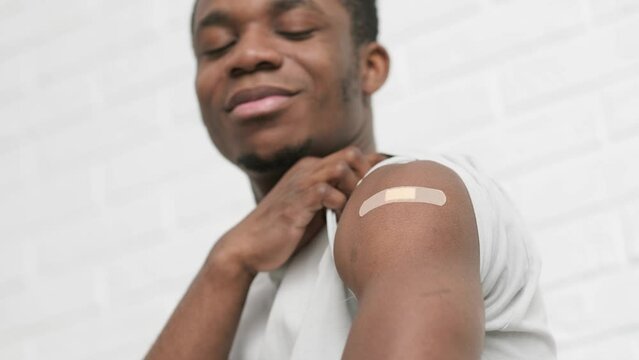 vaccinated African American man showing arm with medical plaster patch Plaster On Shoulder, black male after getting vaccine dose against covid virus, Healthcare immunization, coronavirus vaccination