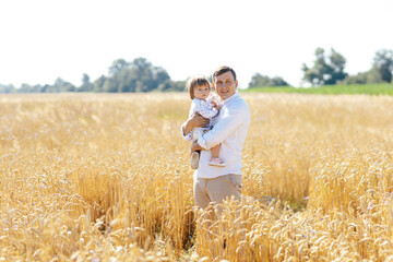 Naklejka na ściany i meble young man with beautiful daughter walking in wheat field. father tenderly touches hir son's hair, holding hands, hugs