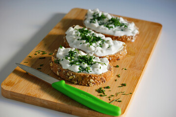 Close-up of three slices of wholemeal bread spread with butter and cottage cheese sprinkled with freshly chopped chives on a bamboo cutting board. Healthy homemade snack concept.