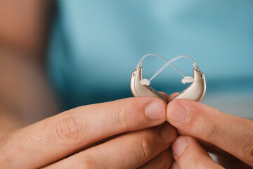 Hearing aids in hands making heart shape over blue background. Closeup of listening device for people with hearing disorder, disfunction. Technology that gives better sense of sound, speach - obrazy, fototapety, plakaty