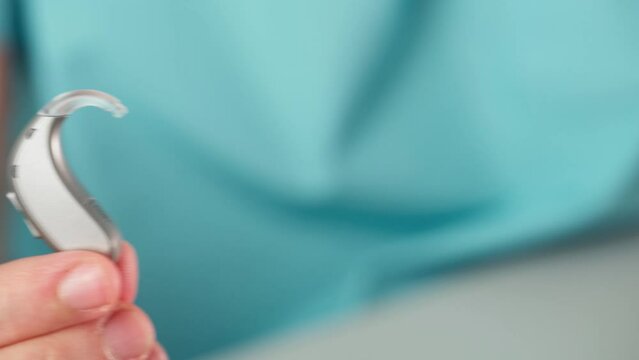 Hearing aids in hands making heart shape over blue background. Closeup of listening device for people with hearing disorder, disfunction. Technology that gives better sense of sound, speach