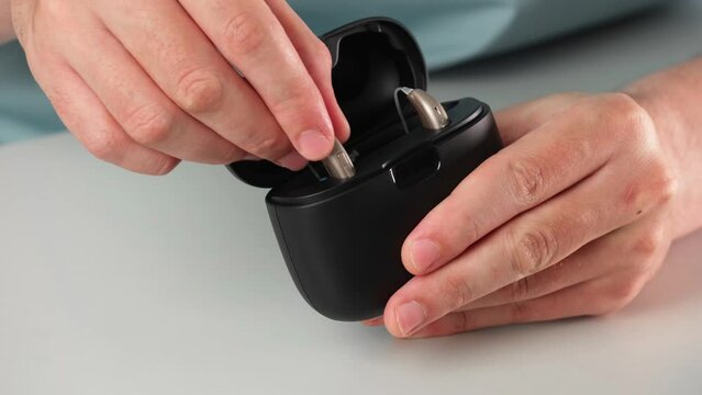 Patient charging hearing aid in special portable Smart Charger with built-in power bank. Case in man hands keeps hearing aids dry and safe