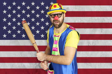 An insecure clown holds a bat in his hands against the background of the flag of USA