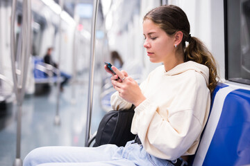 Focused girl riding on a subway train is texting with friends on her mobile phone