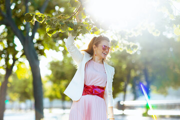 happy modern female in pink dress and white jacket in city