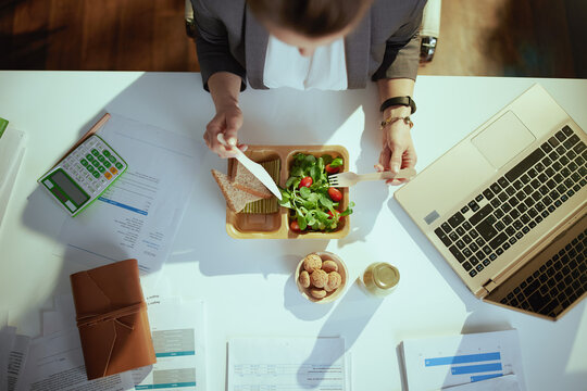 woman worker in grey business suit in green office eating salad