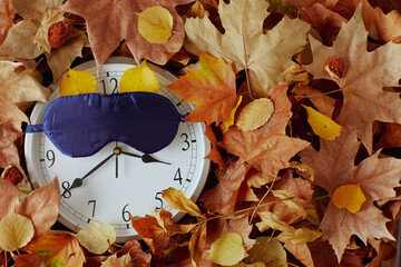 Fototapeta autumn background with clock, sleeping mask and leaves obraz