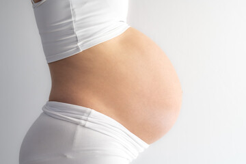 Middle part of unrecognizable standing woman with very round pregnant baby bump. Side view. White background. Bright shot.