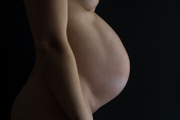 Middle part of unrecognizable standing naked mother with very round pregnant baby bump. Final month of pregnancy - week 36. Side view. Black background.