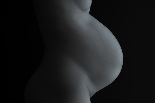 Middle part of unrecognizable standing naked mother with very round pregnant baby belly. Final month of pregnancy - week 36. Side view. Black background. Selen tone.