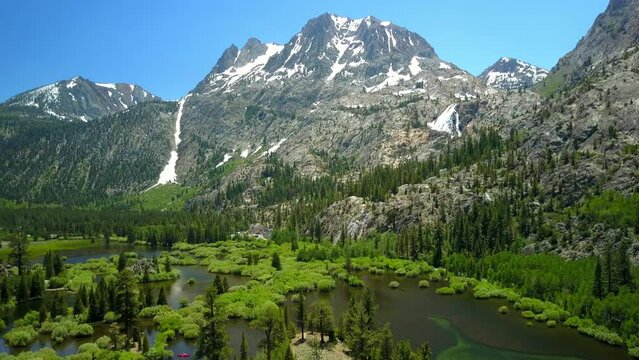 Aerial Shot Of Lake Amidst Green Trees Near Mountains, Drone Flying Forward Over Natural Landscape Against Sky - Mammoth Lakes, California