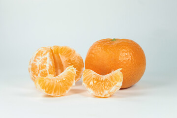 close-up of a tangerine with various wedge  next to it on a white background