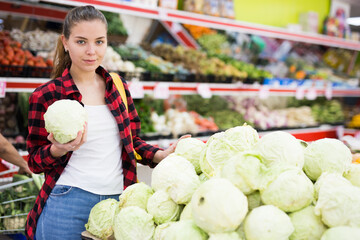 Portrait of a positive customer girl in a store near the counter, holding a cabbage in her hands