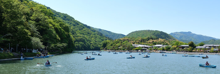 Panoramic landscape of people in rowing boats on Katsura River in Arashiyama, Kyoto, Japan.