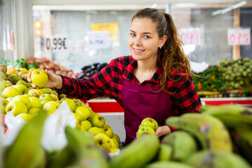 Female shopping assistant selling fresh apples and other fruits in grocery shop