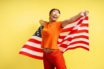 Beautiful smiling African American woman holding American flag isolated on yellow background....