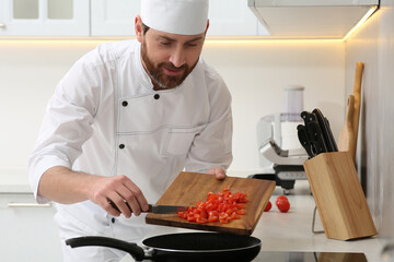 Professional chef putting cut tomatoes into frying pan in kitchen