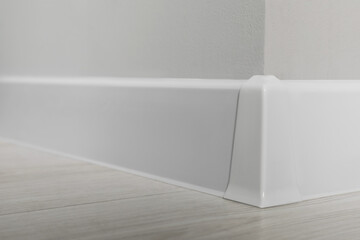 White plinth with connector on laminated floor near wall indoors, closeup