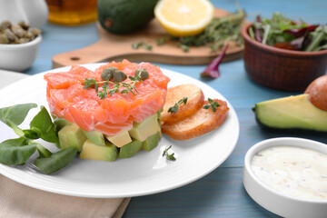 Delicious salmon tartare served with avocado and croutons on light blue table