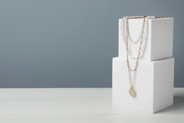 Stylish presentation of necklaces on podiums on white wooden table, space for text