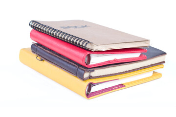 A stack of books with a yellow and red cover and a red notebook on top