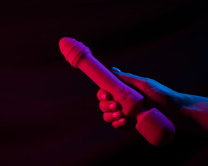 Woman holding a vibrator in neon pink and blue light.