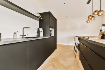 a modern kitchen with wood flooring and black cabinets in the center of the room is a large white wall