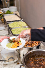 a food buffet with hot dishes and salads on a table being served by a woman's hand