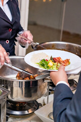 a food buffet with hot dishes and salads on a table being served by a woman's hand