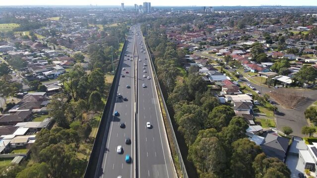 Aerial drone pullback reverse view above the South Western M5 Motorway at Casula in Sydney, NSW Australia with Liverpool CBD in the background 