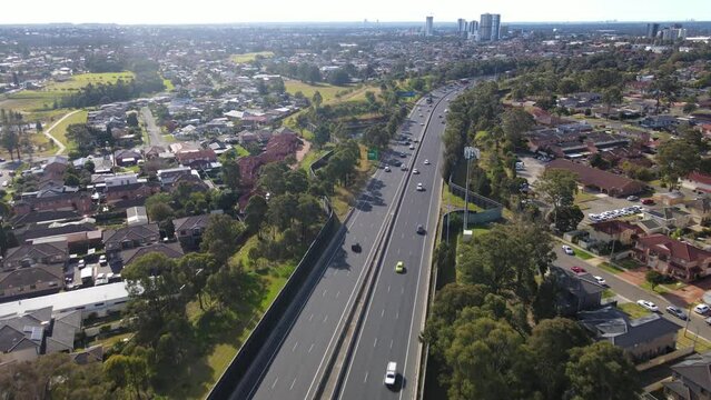 Aerial drone pullback reverse view above the South Western M5 Motorway at Casula in Sydney, NSW Australia with Liverpool CBD in the background 