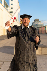 Man recent graduated, dressed in cap and gown, showing off his degree celebrating.