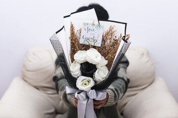 Hand holding beautiful flower bouquet of black and white roses with You Did Great card covering...