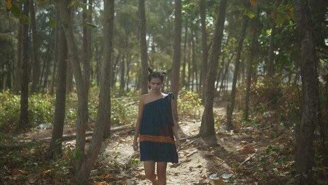 An Indian dressed in a colorful dress, walks through a green and harmonious forest leaving the background blurred.