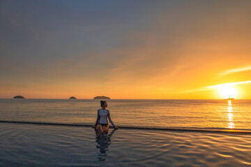 Fototapeta na wymiar Women relaxed in outdoor pool on sunset near the ocean. Summer travel vacation concept, relax in luxury infinity pool.