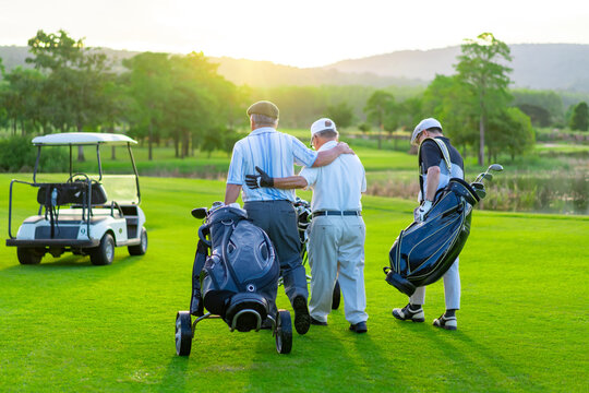 Group of Asian businessman and senior CEO holding golf bag walking on golf course with talking together. Healthy people enjoy outdoor sport lifestyle golfing at country club on summer holiday vacation