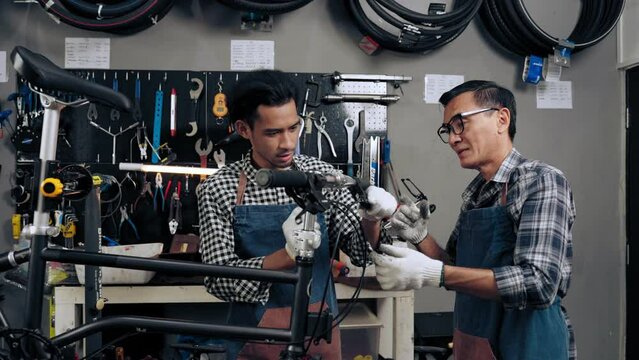 Owner shop bicycle senior man training employee to fixed bike in bike shop. Young man assistant and professional repairman assembling bicycle together in shop. Maintenance and repair Concept