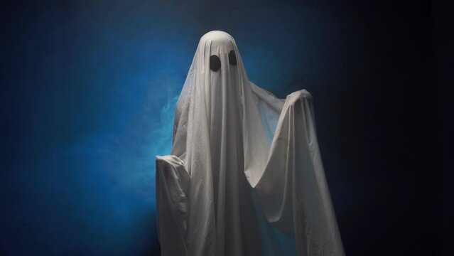 Ghost in sheet dancing in blue smoke over black background